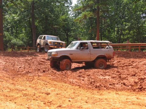 1995 Ford C-350 (Centurion Conversions) - Two Ford Broncos navigate a muddy off-road course during a summer event.