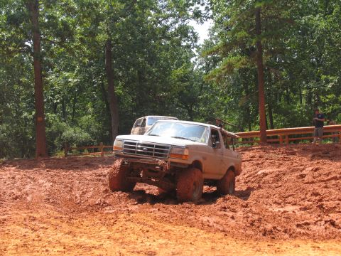 1995 Ford C-350 (Centurion Conversions) - A lifted Ford Bronco tackles a steep, muddy incline surrounded by trees.