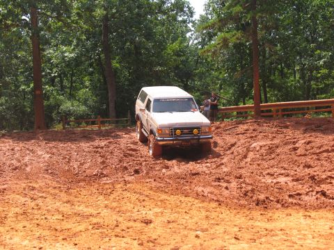 1995 Ford C-350 (Centurion Conversions) - A white SUV navigates a muddy trail, its off-road tires kicking up dirt.