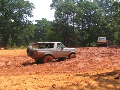 1995 Ford C-350 (Centurion Conversions) - A silver SUV is stuck in thick mud, with another truck visible in the background on a muddy trail.