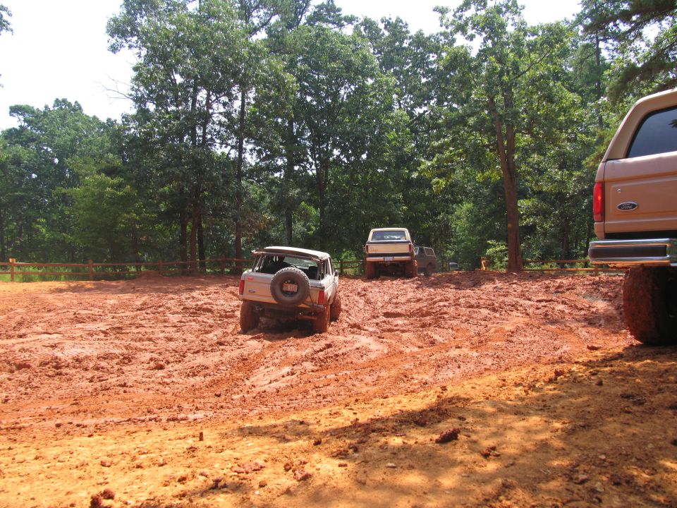Several off-road vehicles navigating a muddy terrain with trees in the background