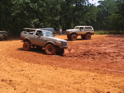 1995 Ford C-350 (Centurion Conversions) - Two off-road vehicles are seen navigating a muddy terrain under a clear sky.