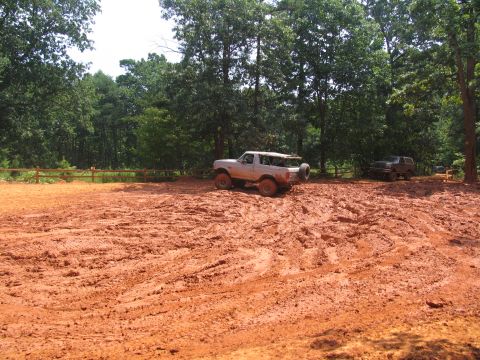 1995 Ford C-350 (Centurion Conversions) - Off-road vehicles navigate a challenging muddy terrain under a canopy of trees.
