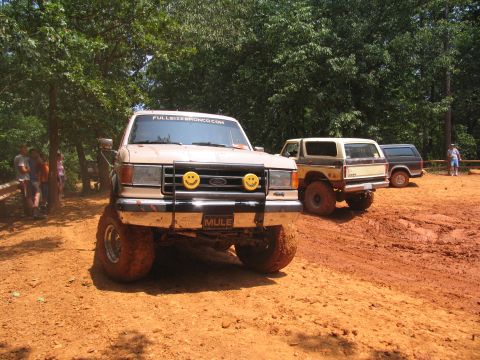 1995 Ford C-350 (Centurion Conversions) - Three off-road vehicles are parked on a dirt track with trees in the background.