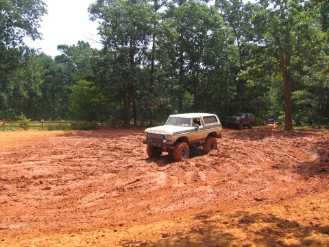 1995 Ford C-350 (Centurion Conversions) - Two SUVs navigate a muddy off-road course surrounded by trees.