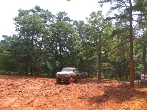 1995 Ford C-350 (Centurion Conversions) - Off-road vehicles navigate a muddy terrain surrounded by trees, with spectators watching on the right.