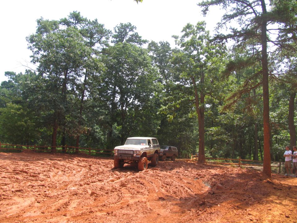 White Ford Bronco with lifted suspension driving through mud, another SUV behind it
