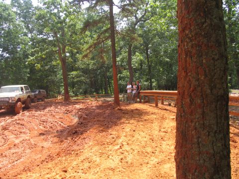 1995 Ford C-350 (Centurion Conversions) - Two off-road vehicles navigate a muddy trail surrounded by trees during an outdoor event.