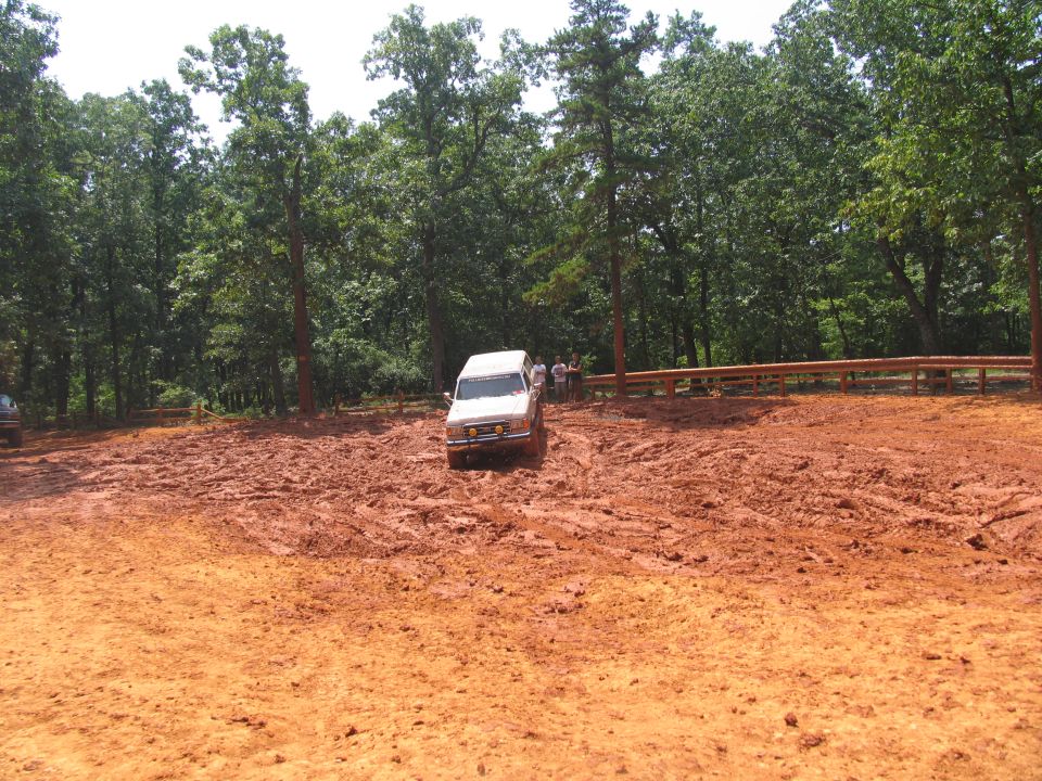 White van navigating a muddy off-road course with trees in the background