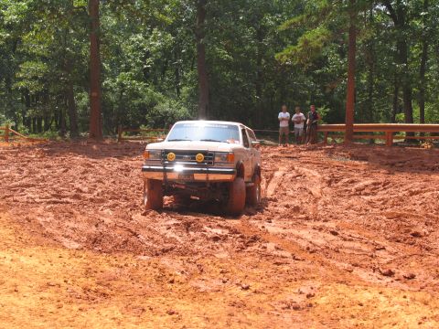 1995 Ford C-350 (Centurion Conversions) - A Ford Bronco II navigates a muddy off-road course with spectators watching.