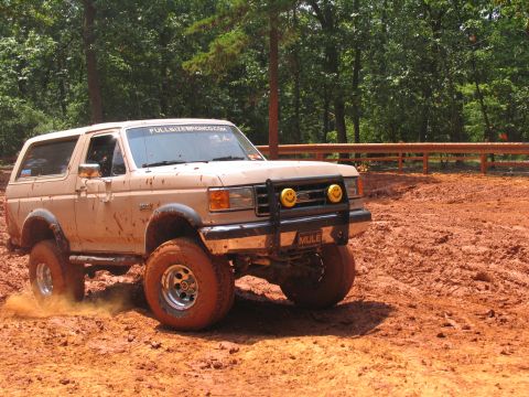1995 Ford C-350 (Centurion Conversions) - Tan Ford Bronco with off-road tires kicks up mud while navigating a dirt track.