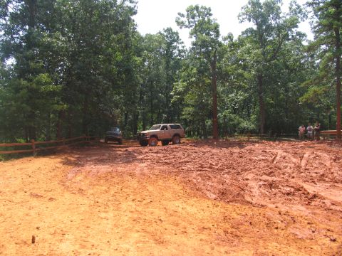 1995 Ford C-350 (Centurion Conversions) - Two SUVs are parked in a muddy clearing surrounded by trees, with a wooden fence in the background.