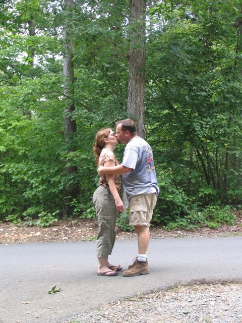1995 Ford C-350 (Centurion Conversions) - Couple shares a kiss on a path in a wooded area.