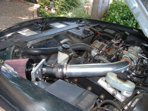 1998 Ford Crown Victoria - Open engine bay of a vehicle showing an aftermarket cold air intake with a polished metal tube and red cone filter.