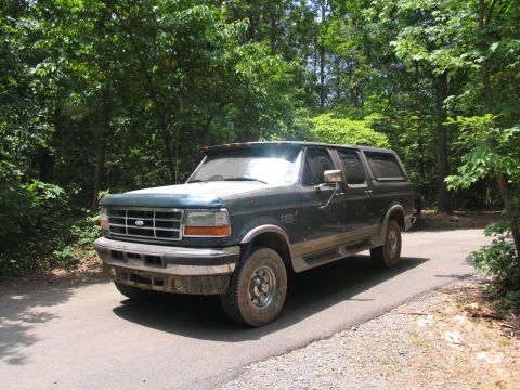 1995 Ford C-350 (Centurion Conversions) - A dark green Ford truck with an extended cab sits on a paved road surrounded by trees.