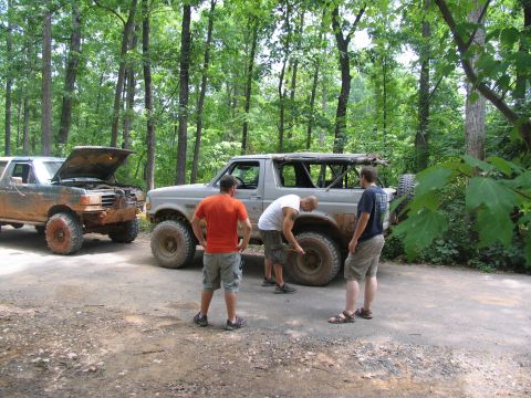 1995 Ford C-350 (Centurion Conversions) - Men work on off-road vehicles in a wooded area during an event.
