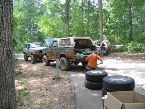 1995 Ford C-350 (Centurion Conversions) - A person works on a green Ford Bronco with its hood open and spare tire mounted on the back, while another Bronco is parked nearby.