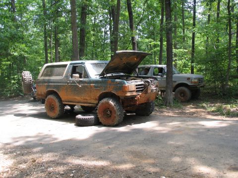 1995 Ford C-350 (Centurion Conversions) - Two off-road vehicles, a Ford Bronco and a Ford truck, are parked on a dirt road in a wooded area.