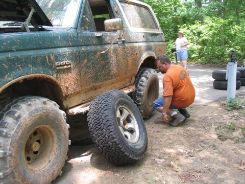 1995 Ford C-350 (Centurion Conversions) - A man kneels to change a flat tire on a muddy green Ford Bronco during an off-road event.