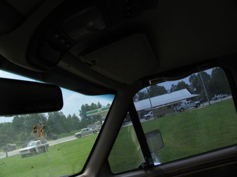1995 Ford C-350 (Centurion Conversions) - View from inside a vehicle shows a trailer being towed by a pickup truck, with a gas station and other vehicles visible in the background.