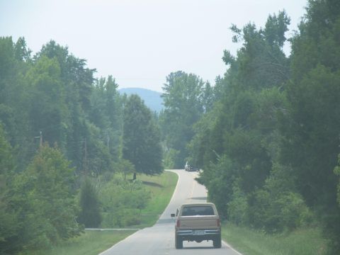 1995 Ford C-350 (Centurion Conversions) - A pickup truck travels down a country road surrounded by trees.