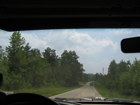 1995 Ford C-350 (Centurion Conversions) - Driving down a country road with trees lining both sides and a cloudy sky overhead.