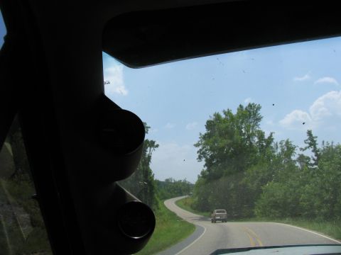 1995 Ford C-350 (Centurion Conversions) - A tan pickup truck travels down a rural, tree-lined road on a sunny day.