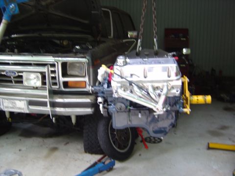 1986 Ford Bronco - A Ford Bronco's front end is visible as its engine is being lowered into place.