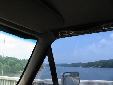 1995 Ford C-350 (Centurion Conversions) - Driving over a bridge with a view of a lake and tree-lined shores on a sunny day.