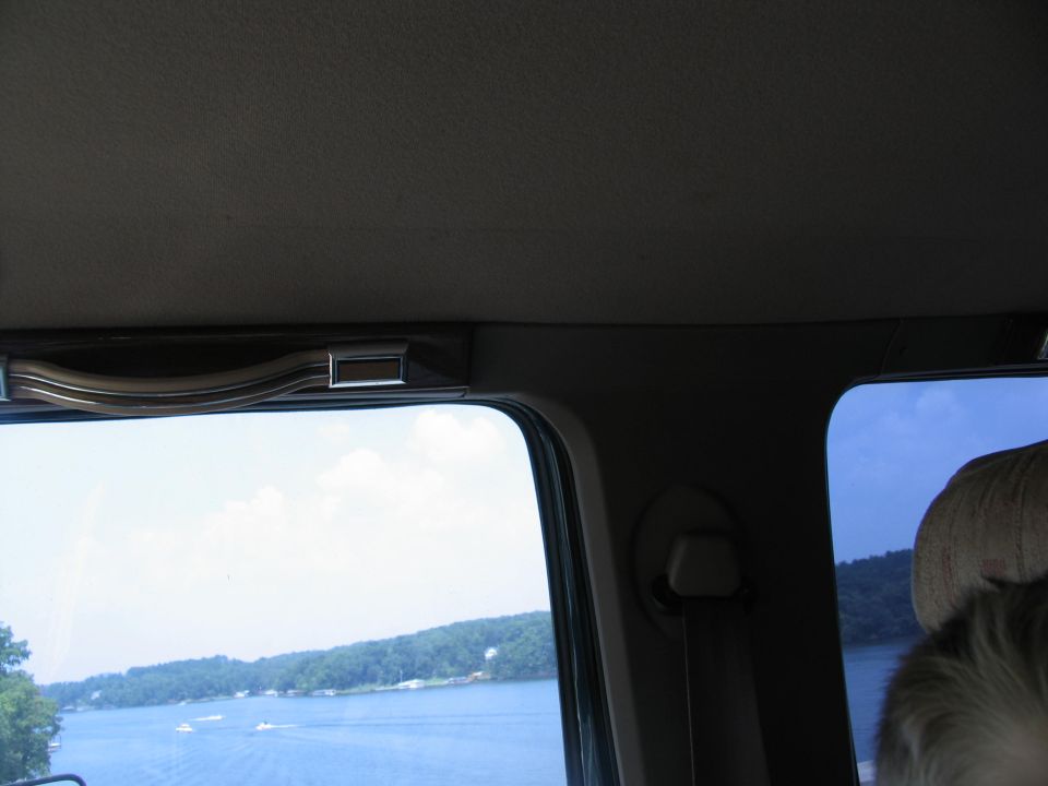 View from inside a vehicle looking out the window at a lake with trees on the shore and boats on the water