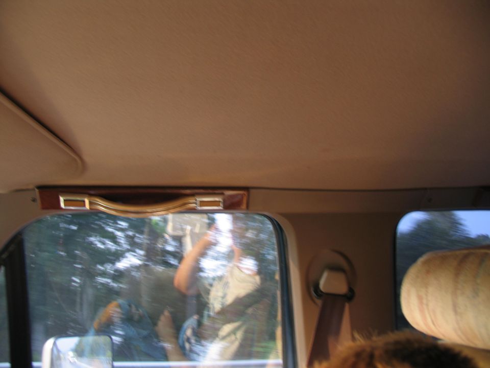 Interior view of a vehicle showing a grab handle, seatbelt, and a reflection of a person in the window