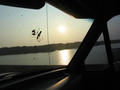 1995 Ford C-350 (Centurion Conversions) - View from inside a vehicle looking out the windshield at a sunset over a lake, with smudges on the glass.
