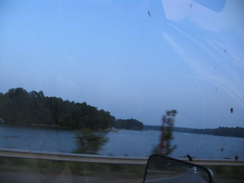 1995 Ford C-350 (Centurion Conversions) - A scenic view of a lake and tree-lined shore, captured from inside a moving vehicle.