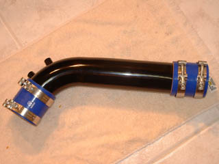 1998 Ford Crown Victoria - black curved metal intake tube fitted with blue silicone couplers and worm-gear clamps, laid on a tile floor.