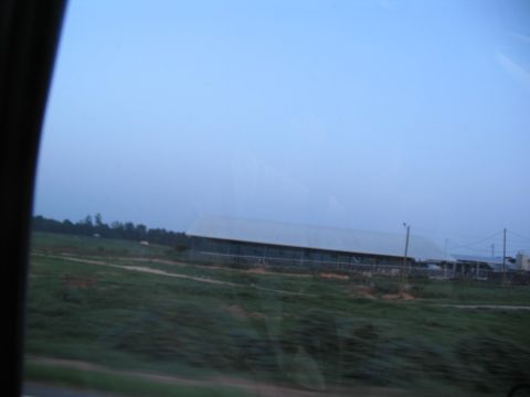 1995 Ford C-350 (Centurion Conversions) - Farm buildings and fields seen from a car window during the day.