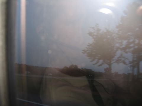 1995 Ford C-350 (Centurion Conversions) - View through a window shows a reflection of trees and sky over a blurry landscape.
