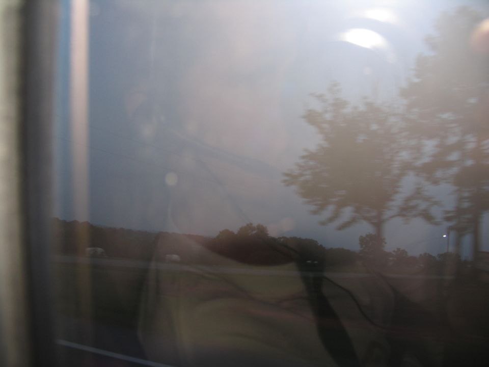 Reflection of trees and sky in a window, with a blurry landscape outside