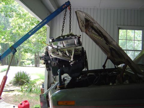 1986 Ford Bronco - Engine hoist lowering a V8 engine into a vehicle bay. Hood is open, showing engine compartment.