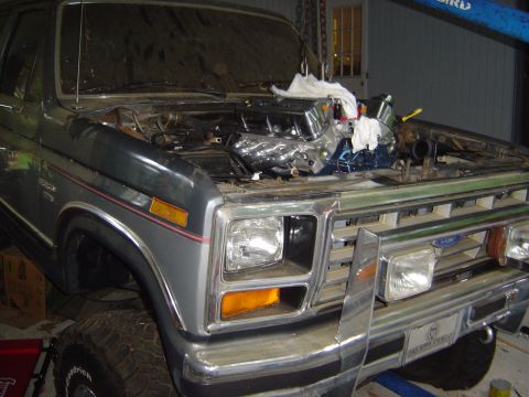 1986 Ford Bronco - A Ford Bronco's engine bay is shown as a new engine is being installed with the help of a hoist.