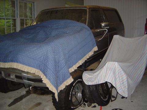 1986 Ford Bronco - A dark SUV is partially covered by blankets in a garage.