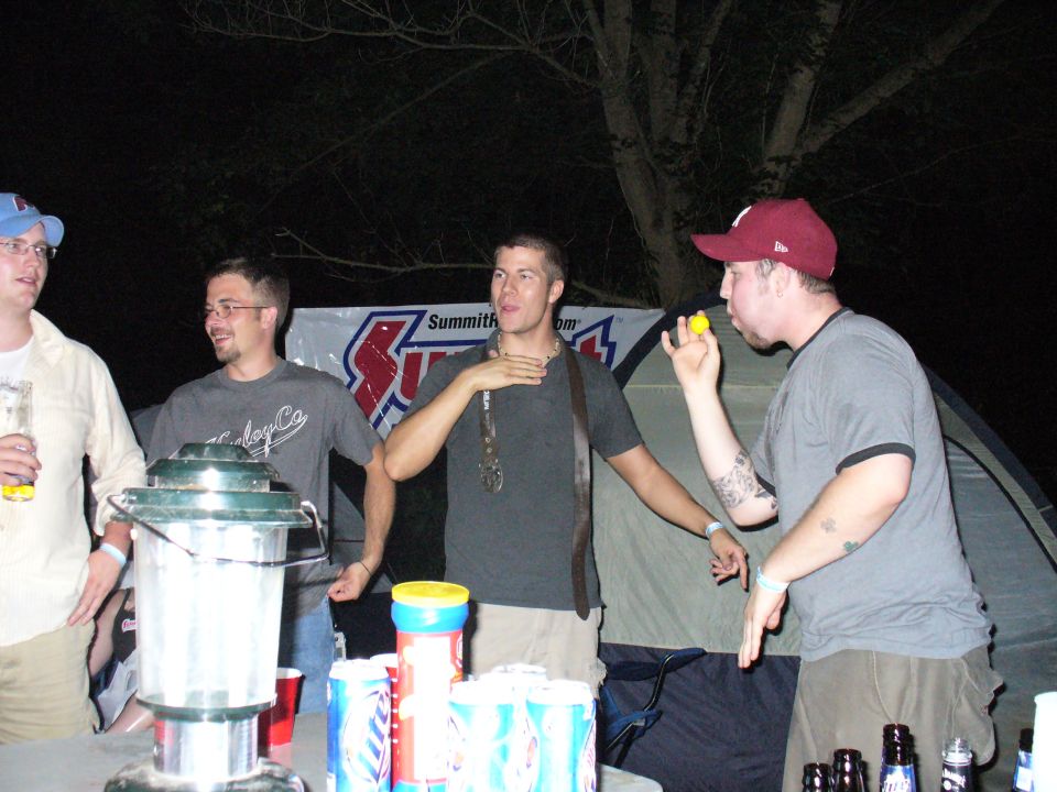 Four guys hanging out at a campsite at night, one blowing a yellow object