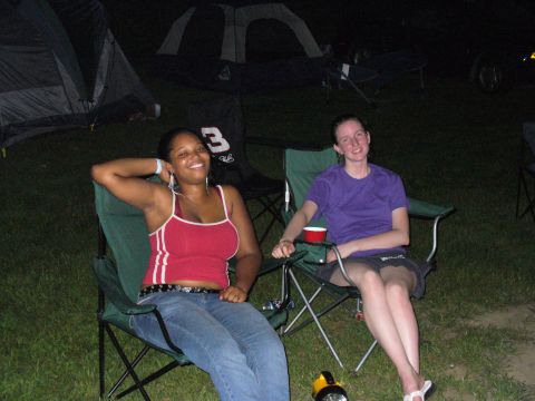 1991 Ford Probe - Two women relax in camping chairs at night, with tents set up behind them.