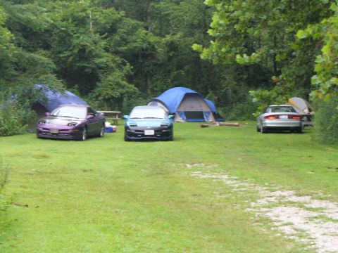 1991 Ford Probe - Three cars are parked at a campsite with tents in the background. The purple car on the left appears to be a 1991 Ford Probe.
