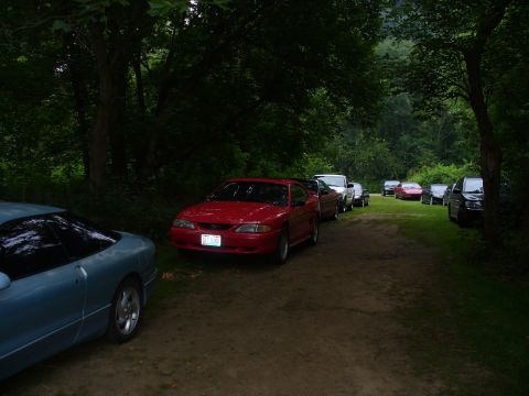 1991 Ford Probe - A blue coupe is parked in the foreground next to a red 1991 Ford Probe, with several other vehicles lined up on a dirt road.