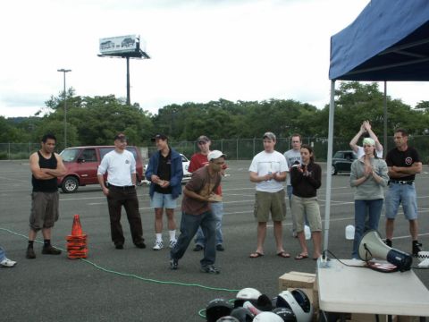 2001 Mercury Grand Marquis - A group of people gather in a parking lot, with a red van and a large billboard visible in the background.