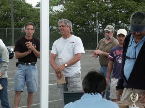 2001 Mercury Grand Marquis - Men gather outdoors, some clapping, near a white pole, with trees and a fence in the background.