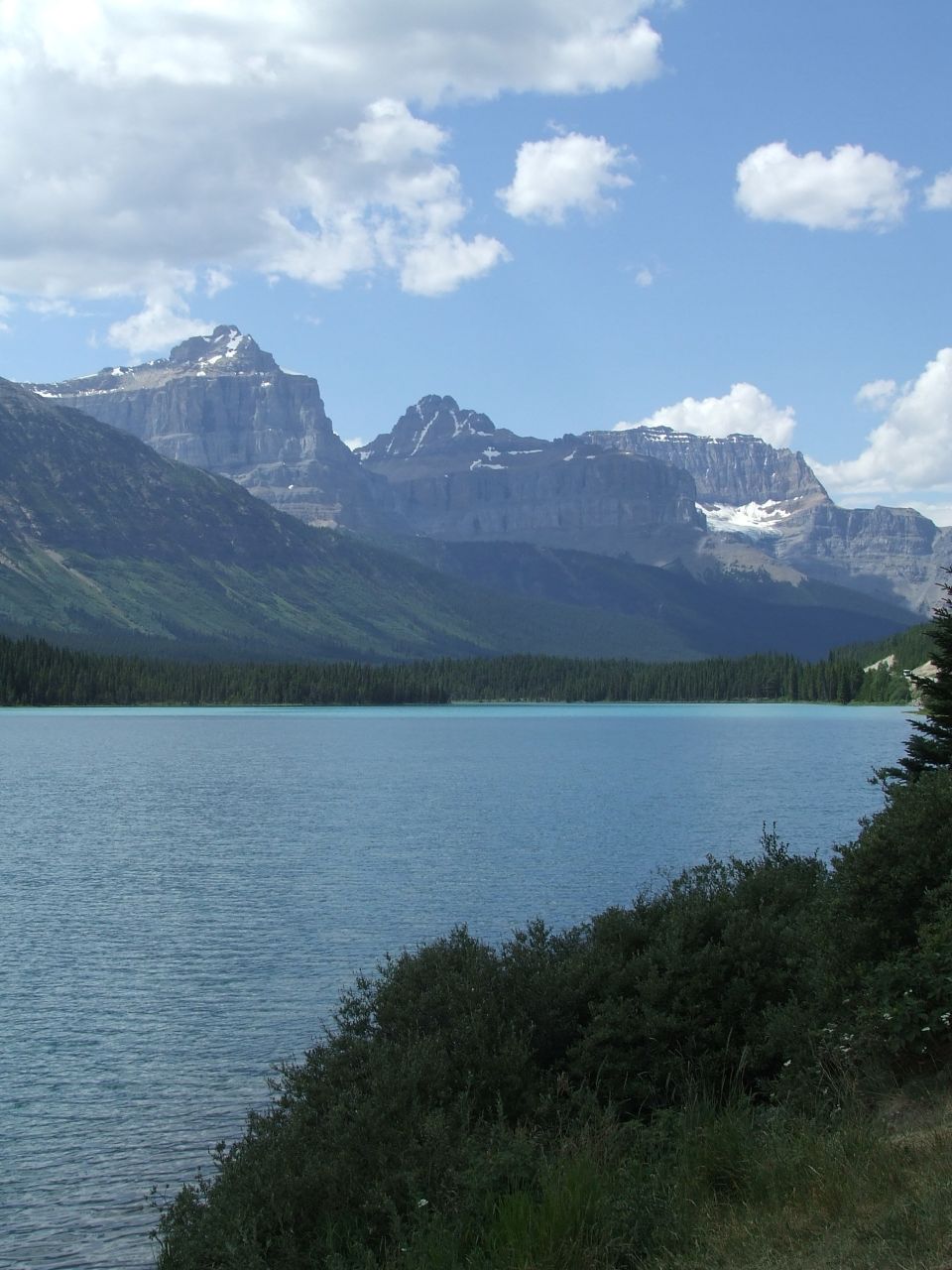 Mountain range overlooking a blue lake with trees and clouds