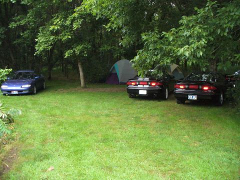 1991 Ford Probe - Three coupes are parked on a grassy area with tents and trees in the background.
