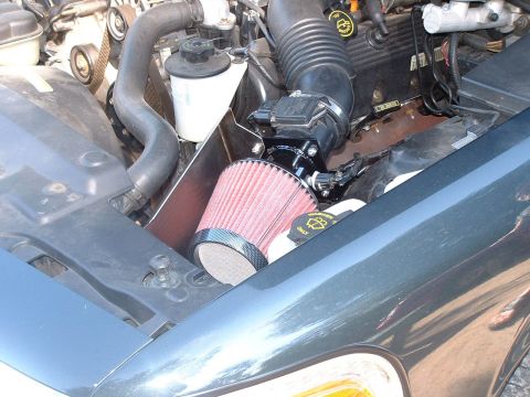 1998 Ford Crown Victoria - Close-up of a red conical performance air filter connected to the intake of an engine in a dark-colored car's engine bay.