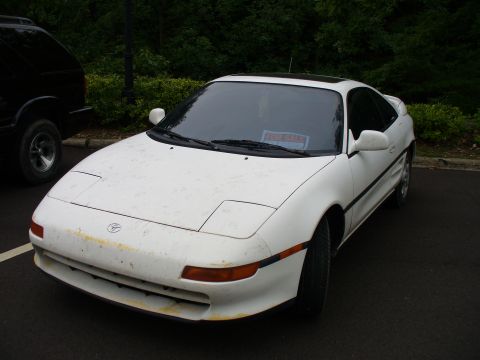 1991 Ford Probe - A white Toyota MR2 is parked in a lot, with a 'For Sale' sign visible on the dashboard.